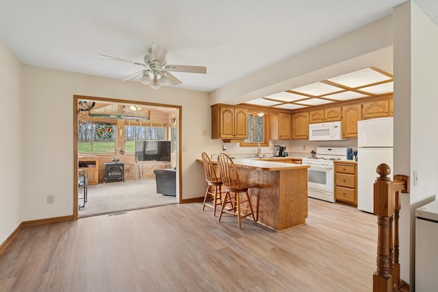 kitchen featuring a wood stove, a peninsula, white appliances, ceiling fan, and a sink