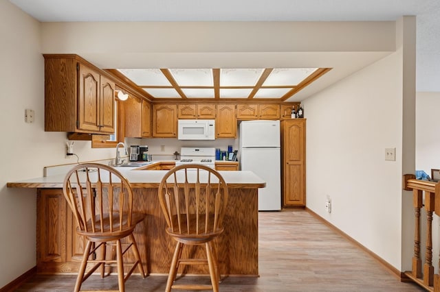 kitchen with brown cabinetry, a sink, a peninsula, white appliances, and light wood-style flooring