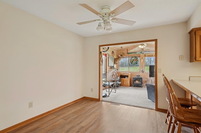 dining room featuring ceiling fan, light wood finished floors, a wood stove, baseboards, and visible vents