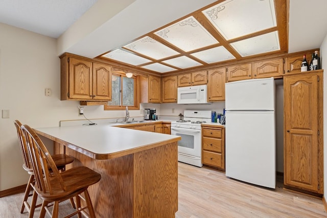kitchen featuring a peninsula, white appliances, a breakfast bar, a sink, and light wood-style flooring