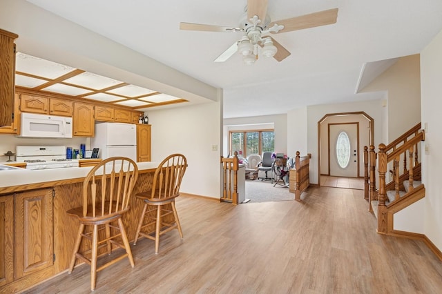 kitchen with a breakfast bar, white appliances, baseboards, light wood-type flooring, and light countertops