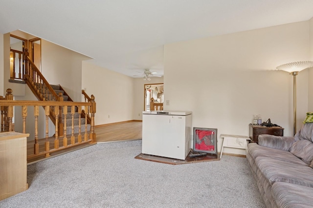 living area with carpet floors, ceiling fan, baseboards, and stairs