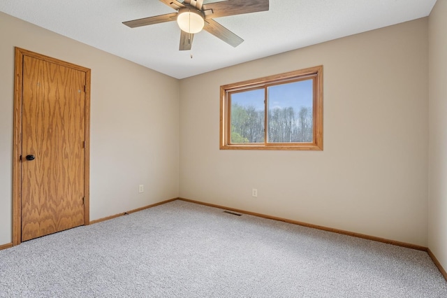 carpeted empty room with baseboards, a ceiling fan, and visible vents
