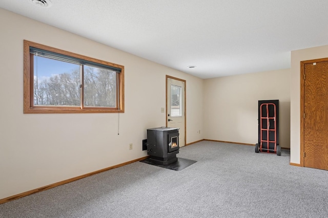 empty room with baseboards, a wood stove, and carpet flooring