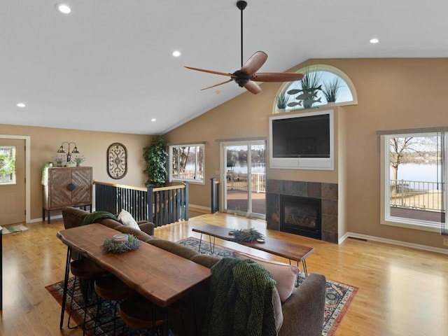 living area with a tiled fireplace, ceiling fan, healthy amount of natural light, high vaulted ceiling, and baseboards