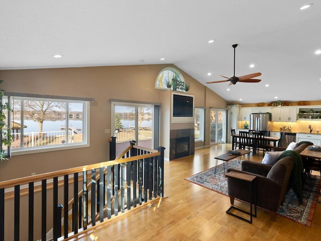living room with ceiling fan, a tile fireplace, light wood-style flooring, high vaulted ceiling, and recessed lighting
