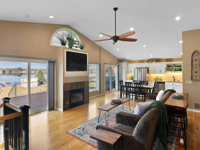 living area featuring ceiling fan, a tile fireplace, light wood-style floors, high vaulted ceiling, and recessed lighting