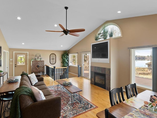 living area with light wood-style flooring, a ceiling fan, a tiled fireplace, recessed lighting, and high vaulted ceiling