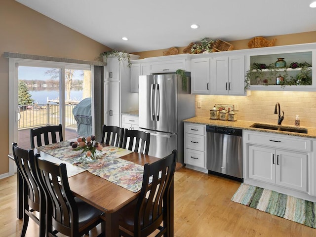 kitchen with stainless steel appliances, a sink, vaulted ceiling, tasteful backsplash, and white cabinets