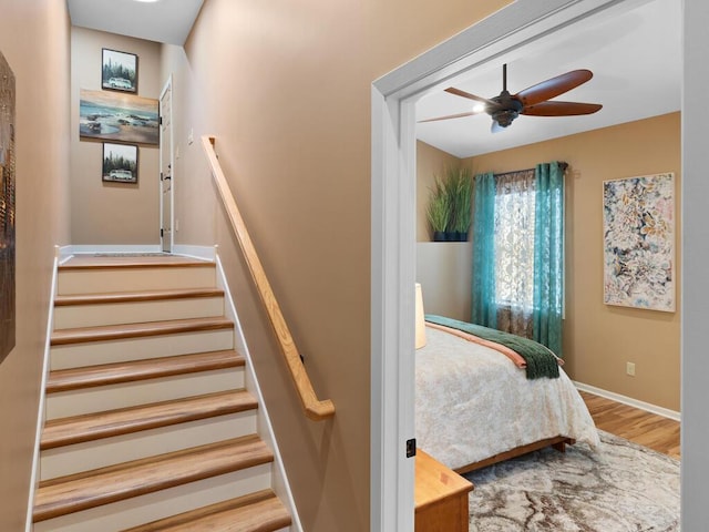 stairway with wood finished floors, ceiling fan, and baseboards