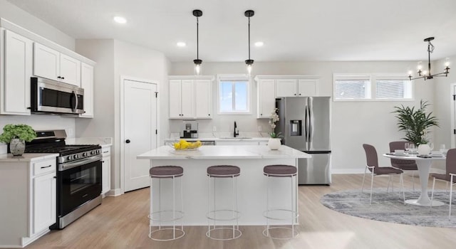 kitchen with light wood-style flooring, white cabinets, a center island, appliances with stainless steel finishes, and a sink