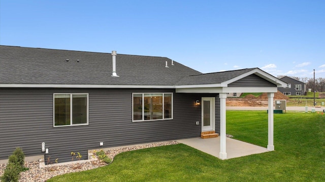 back of property with a shingled roof, a patio, and a lawn