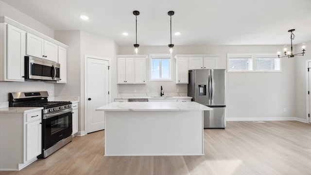 kitchen with an inviting chandelier, a center island, white cabinets, stainless steel appliances, and a sink