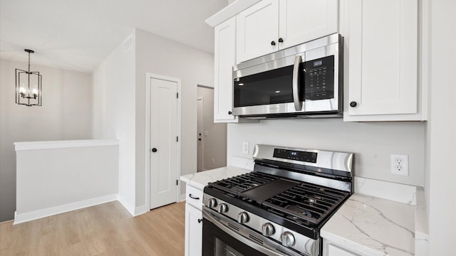 kitchen featuring stainless steel appliances, a notable chandelier, white cabinets, and light stone counters