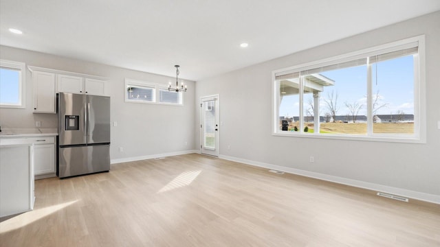 kitchen featuring stainless steel fridge with ice dispenser, white cabinetry, visible vents, light countertops, and a notable chandelier