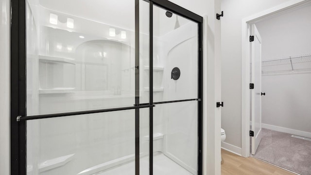 full bathroom with baseboards, a stall shower, toilet, a walk in closet, and wood finished floors
