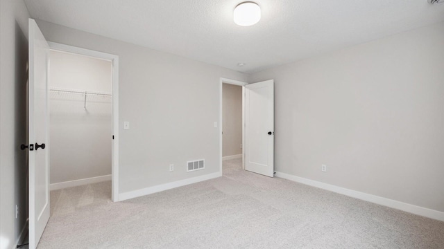 unfurnished bedroom with a spacious closet, visible vents, light carpet, and baseboards