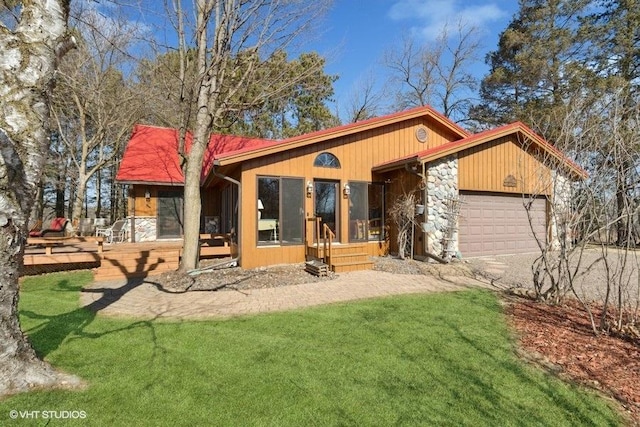 rear view of house with a lawn, stone siding, and an attached garage