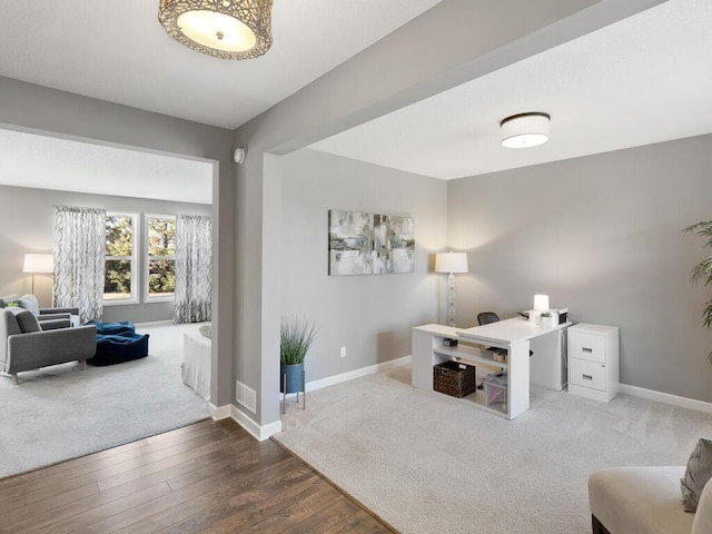 carpeted office with visible vents, baseboards, and wood finished floors