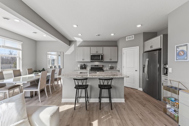 12678 Erskin St NE, Blaine, MN 55449 - kitchen with appliances with stainless steel finishes, light wood-style floors, recessed lighting, light stone countertops, and a kitchen island with sink