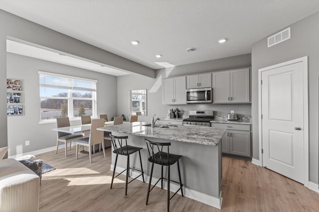 12678 Erskin St NE, Blaine, MN 55449 - kitchen with stainless steel appliances, a sink, a kitchen bar, light wood-style flooring, and recessed lighting
