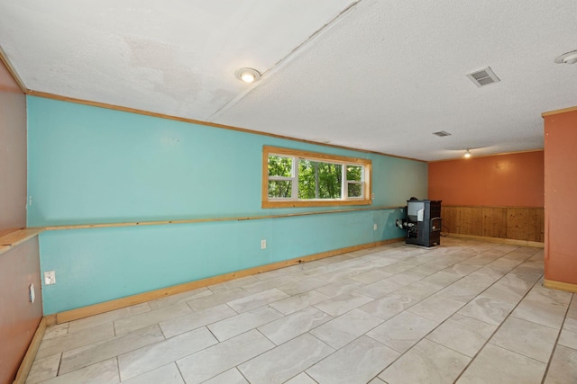 4963 Crofoot Ave NW, Buffalo, MN 55313 - empty room featuring a wood stove, a wainscoted wall, a textured ceiling, wooden walls, and crown molding