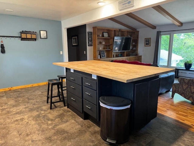 kitchen with a center island, lofted ceiling with beams, dark cabinetry, butcher block countertops, and a breakfast bar area