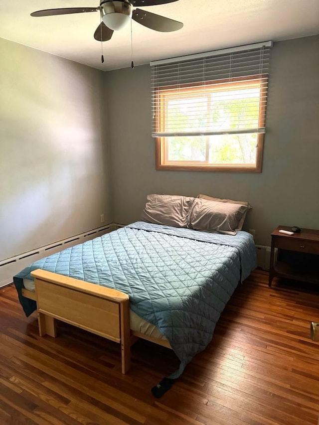 bedroom featuring hardwood / wood-style floors, a baseboard heating unit, and a ceiling fan