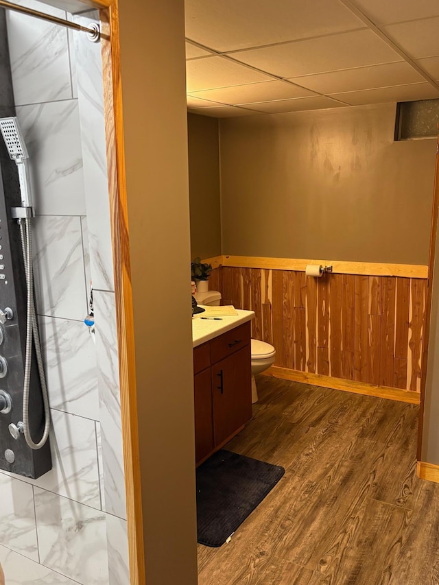 full bathroom with vanity, walk in shower, toilet, wainscoting, and a drop ceiling