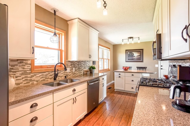 kitchen with white cabinets, rail lighting, a sink, appliances with stainless steel finishes, and decorative light fixtures