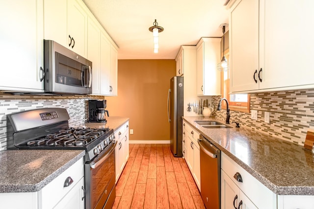 kitchen featuring a sink, light wood-style flooring, stainless steel appliances, baseboards, and white cabinetry