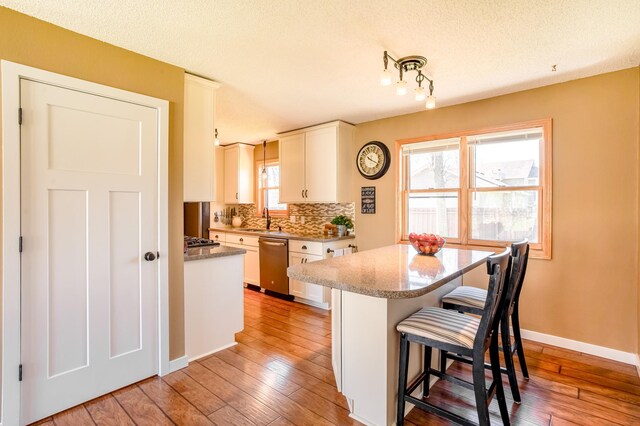 kitchen featuring white cabinets, a sink, a kitchen breakfast bar, backsplash, and stainless steel dishwasher
