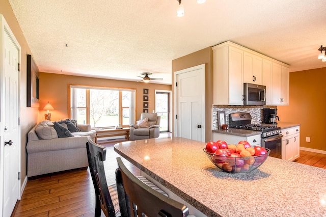 kitchen with backsplash, appliances with stainless steel finishes, white cabinets, wood-type flooring, and open floor plan
