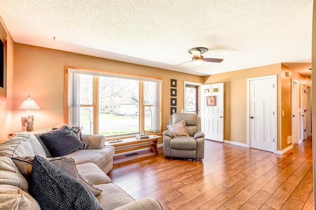 living room featuring light wood-type flooring, a textured ceiling, ceiling fan, and baseboards