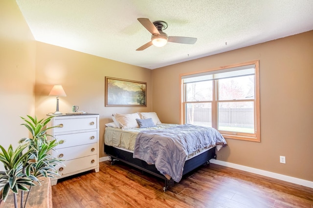 bedroom featuring baseboards, a textured ceiling, ceiling fan, and wood finished floors