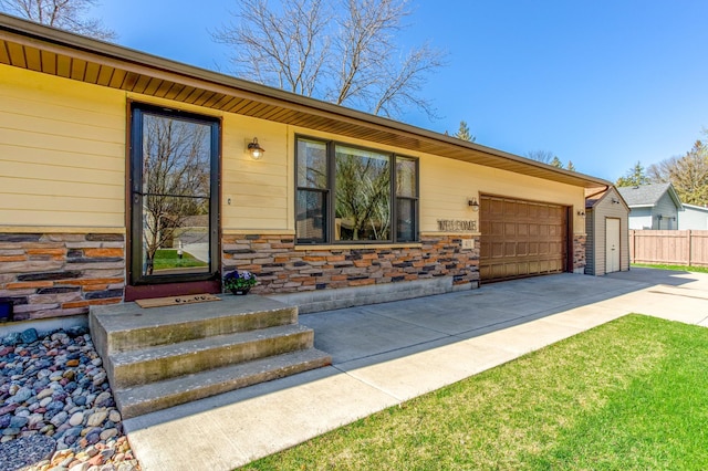 property entrance featuring an attached garage, fence, driveway, and stone siding