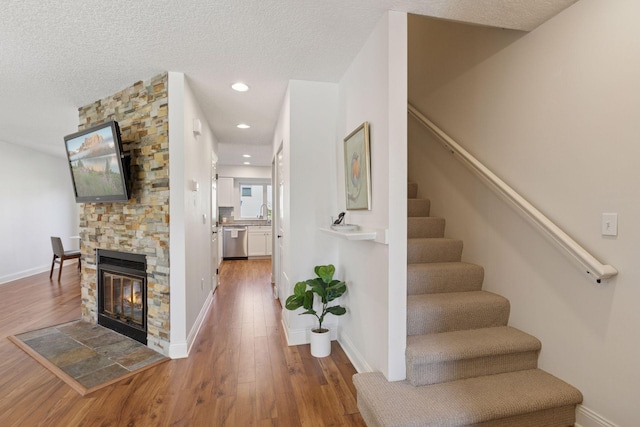 stairway featuring wood finished floors, a stone fireplace, baseboards, a textured ceiling, and recessed lighting