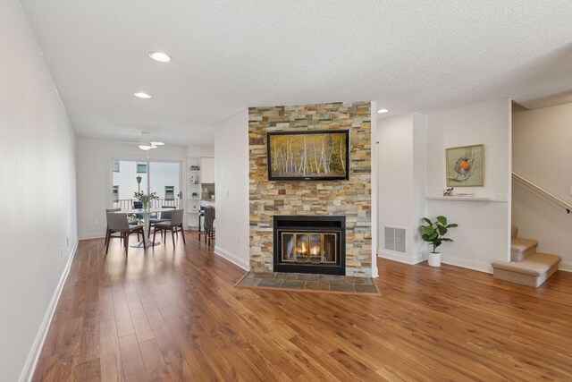 living area with wood finished floors, stairs, baseboards, a stone fireplace, and recessed lighting