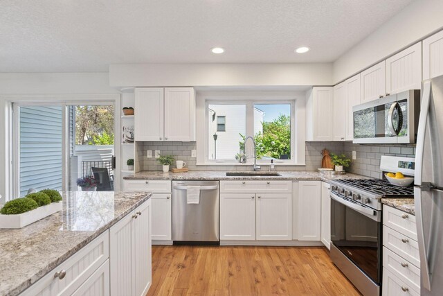 kitchen featuring stainless steel appliances, a sink, light wood-style floors, white cabinets, and a textured ceiling