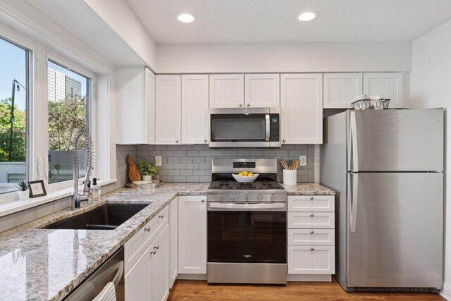 kitchen with stainless steel appliances, a sink, white cabinets, light stone countertops, and decorative backsplash