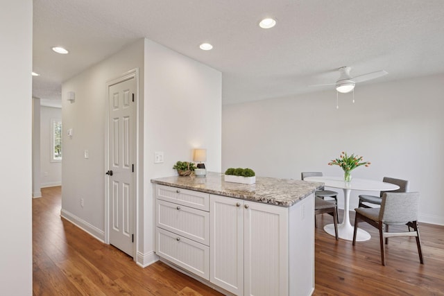 kitchen with wood finished floors, white cabinets, a ceiling fan, light stone counters, and baseboards