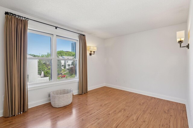 spare room featuring light wood-type flooring, baseboards, and a textured ceiling