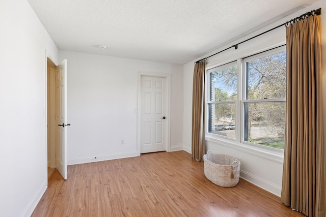 spare room with light wood-style floors, baseboards, and a textured ceiling