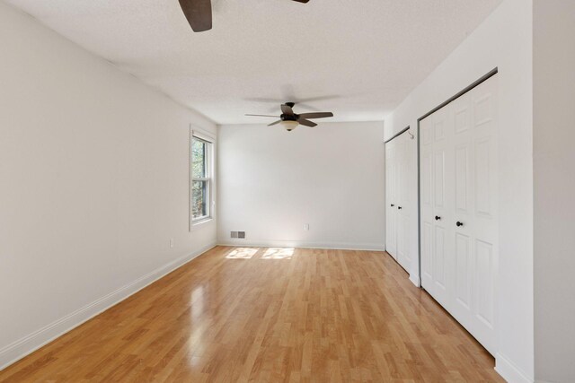 unfurnished bedroom featuring light wood-style flooring, multiple closets, baseboards, and a ceiling fan