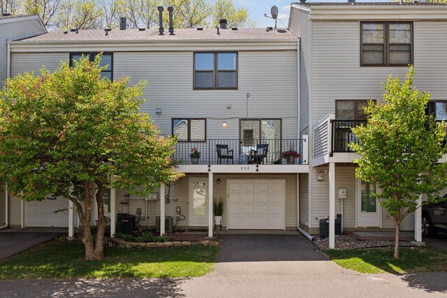 view of front facade featuring an attached garage, central AC unit, driveway, and a balcony