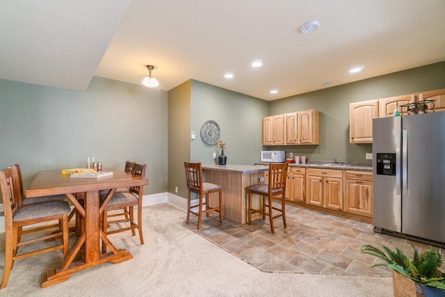 kitchen with white microwave, light brown cabinetry, a sink, stainless steel refrigerator with ice dispenser, and a kitchen breakfast bar