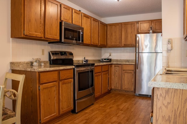 kitchen with tasteful backsplash, appliances with stainless steel finishes, brown cabinetry, and light wood-type flooring