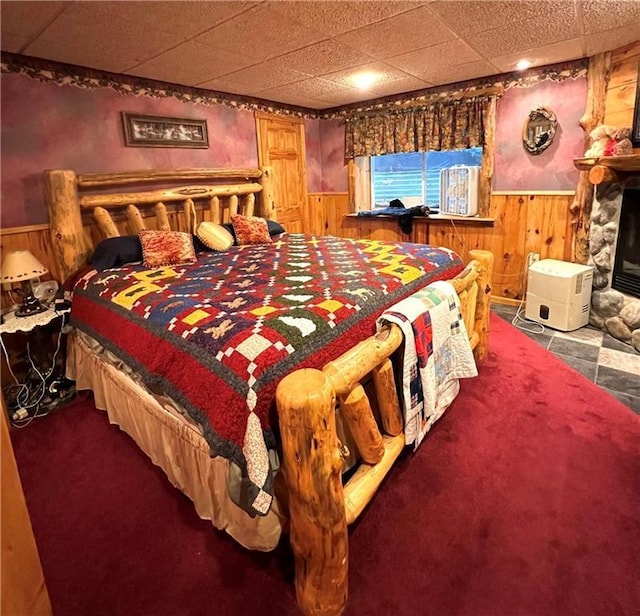 carpeted bedroom featuring wooden walls, a glass covered fireplace, and wainscoting