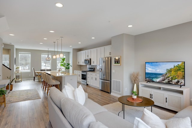 living room with visible vents, baseboards, recessed lighting, and light wood finished floors