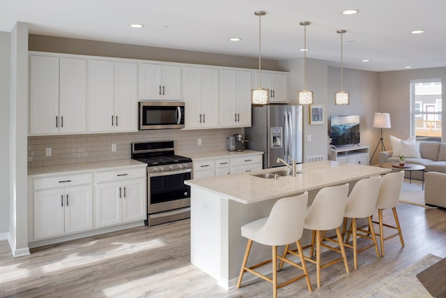 kitchen with a sink, open floor plan, a center island with sink, backsplash, and stainless steel appliances